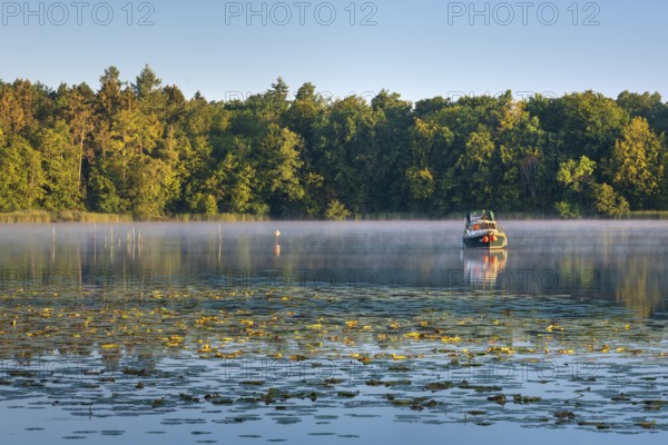 Morning atmosphere at Lake Grienerick, boat anchored, morning mist on the water, water lilies in
