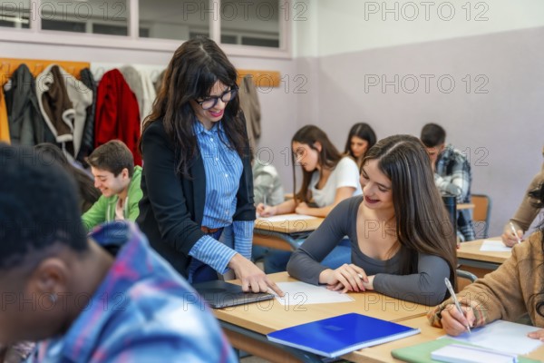 Female professor assisting a smiling student with her exam paper in a classroom full of diverse