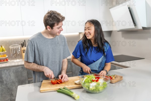 Asian woman and caucasian man enjoying quality time in a modern kitchen, chopping vegetables and