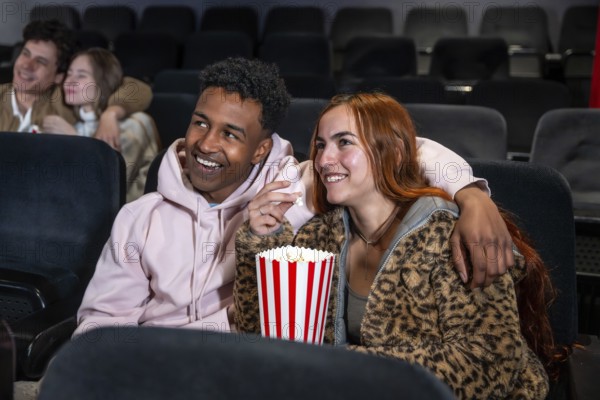Happy couple sharing popcorn while watching a movie at the cinema, enjoying a night out with