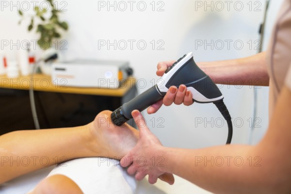 Close-up of an unrecognizable patient on stretcher receiving a shockwave therapy massage on foot in