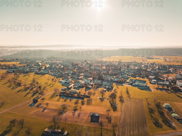 View of a village surrounded by fields and trees in the warm autumn light, Neubulach, Black Forest,