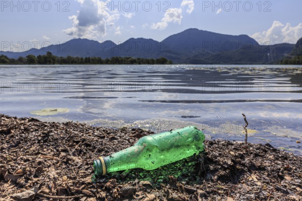 Empty beer bottle lying on the shore of a lake, rubbish, pollution, sunny, Lake Kochel, behind it
