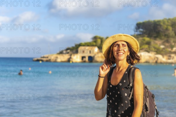 Female tourist with backpack and straw hat enjoying summer holidays on beautiful s'amarador beach