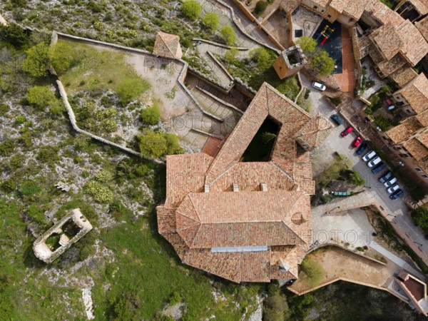 An aerial view of a historic fortress with tiled roofs and surrounding buildings on stony terrain,