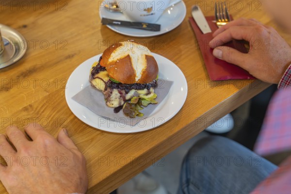 A burger on a pretzel bun is served on a table in the restaurant, autumn creations, Cafe Kuh,