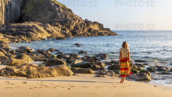 A woman on a sandy beach in Nanjizal Bay. Evening, golden hour. St Just, Penzance, Cornwall,
