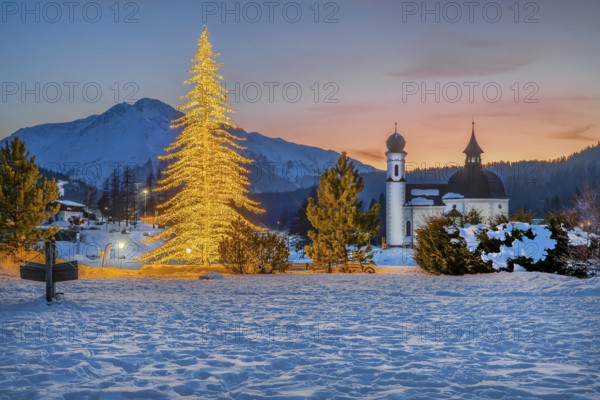 Seekirchl with artificially illuminated winter fir tree and Hocheder 2797m at dusk in winter,