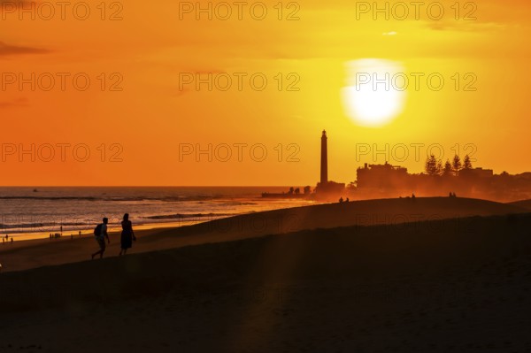 Tourists walking on the maspalomas dunes at sunset, with the maspalomas lighthouse in the