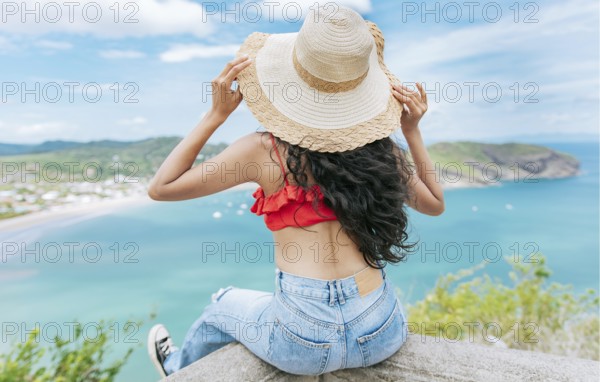 Rear view tourist girl sitting at a viewpoint looking at the beach. Back view of woman on vacation