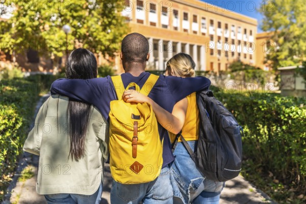 Rear view of three multi-ethnic students embracing while walking together to the university