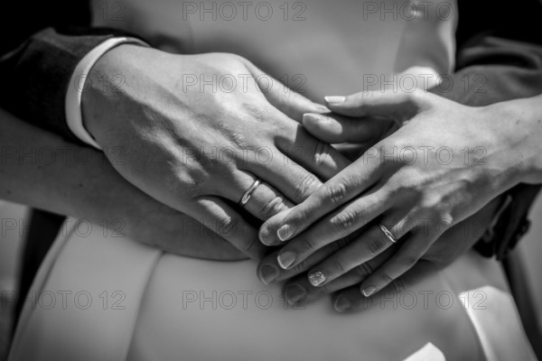 A couple is embracing each other with their hands clasped, and both are wearing wedding rings.