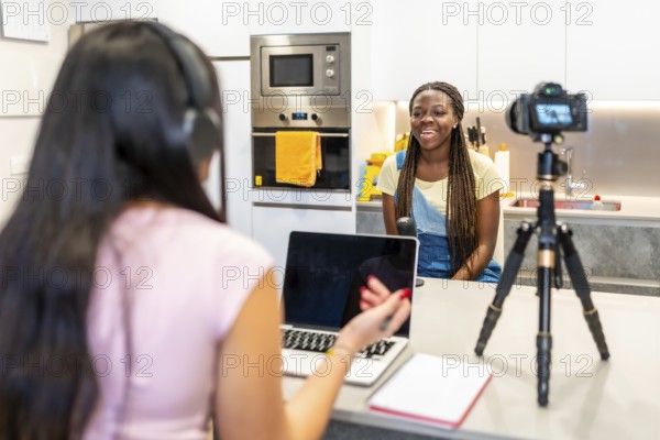 Two teenage girls creating content for their video blog, recording with a camera and using a laptop