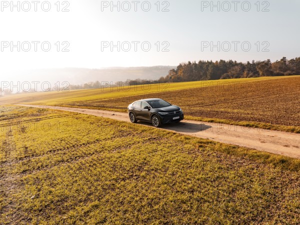 A black car on a dirt road in the middle of golden autumnal fields in sunlight, electric car VW