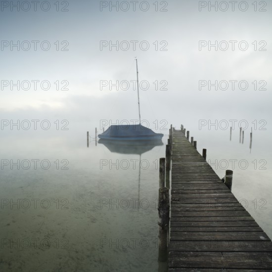 Quiet autumn morning on Lake Chiemsee, jetty with sailing boat in dense fog, Prien am Chiemsee,
