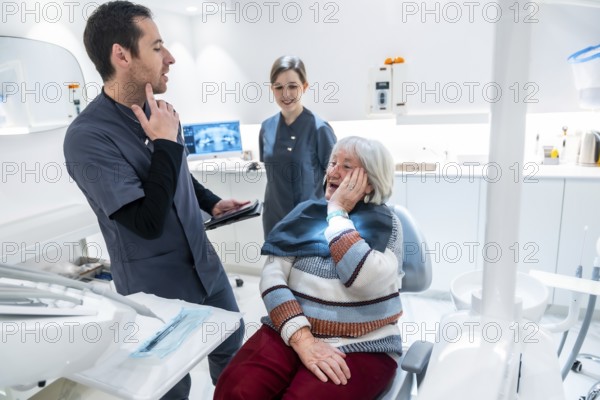 Senior woman suffering from toothache discussing treatment options with dentist and nurse in a