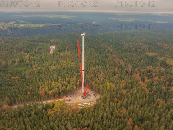 A tall crane erects a wind turbine in the dense autumn forest, wind farm construction site,