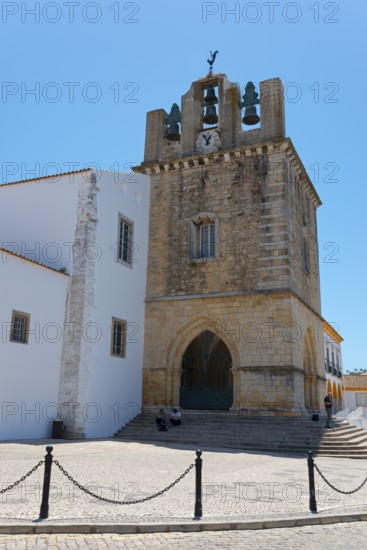 Historic church with bell tower, surrounded by white buildings, under a bright blue sky, Sé