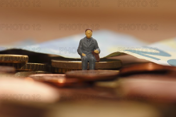 Miniature man sitting on euro coins, twenty euro note in the background, North Rhine-Westphalia,