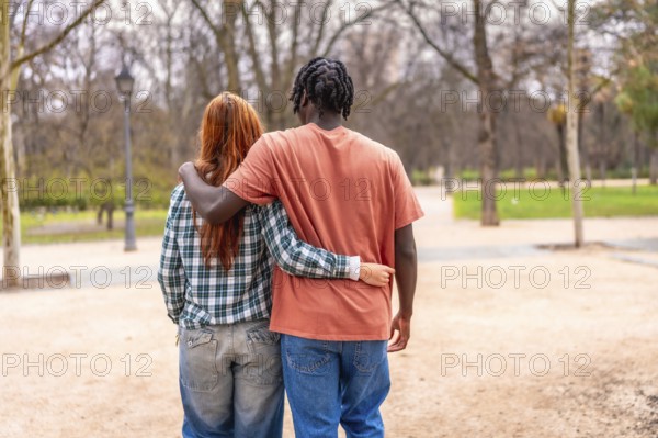 Young multi ethnic couple walking together in a park with arms around each other, enjoying a