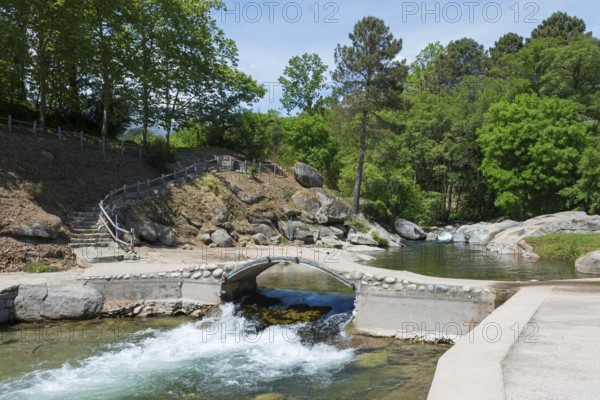 Ein friedlicher Fluss mit einer kleinen Brücke und steinernen Stufen, eingebettet in eine grüne