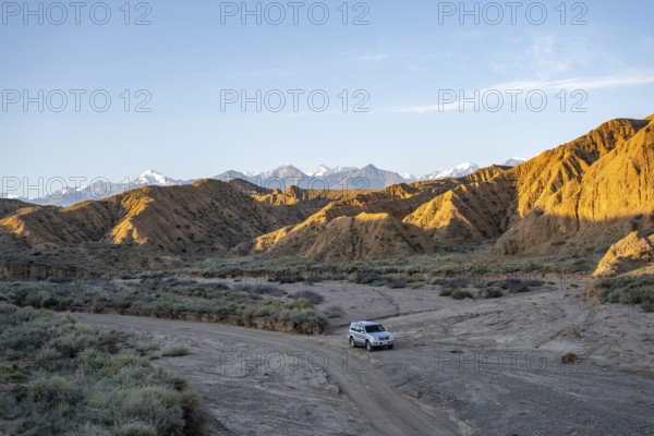 Off-road vehicle driving through a canyon, landscape of eroded hills at sunrise, badlands, white