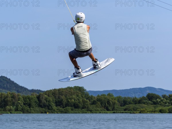 Young man jumping with wakeboard over jump and obstacle, water sports, water skiing in wakepark,