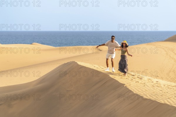 Couple running down sand dunes at maspalomas with ocean in background enjoying summer vacation in
