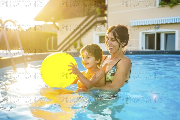 Mother and son having fun together in a home swimming pool, playing with a yellow inflatable ball