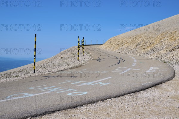 Winding road on a barren hill under a clear blue sky with yellow posts at the edge, Mont Ventoux,