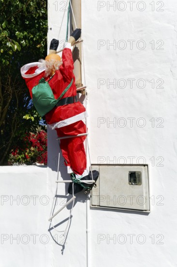 Artificial Father Christmas with rucksack, climbs up ladder, white house facade, funny decoration,