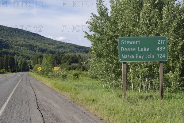 Narrow, traffic-free road leads through forest landscape, sign with huge distances, wilderness,