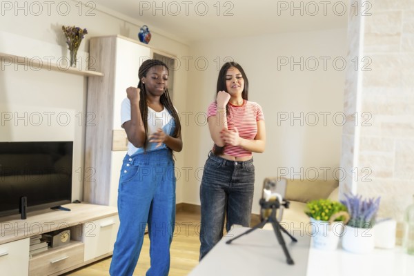 Two female friends dancing joyfully at home, capturing their fun moments on a smartphone while