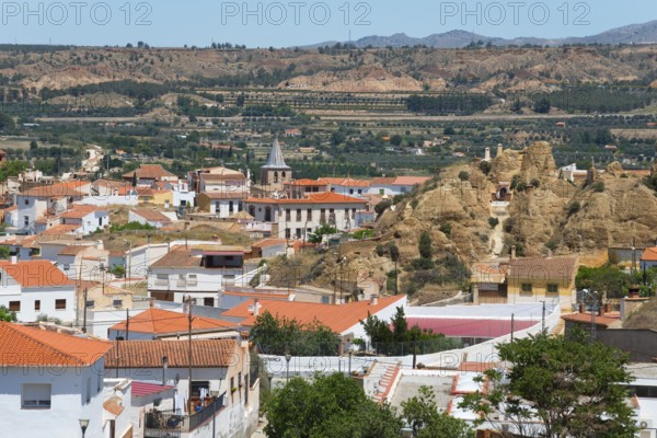 Panoramic view of a village with red roofs and mountains in the background under a clear sky, cave