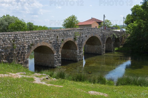 Stone bridge over river, flanked by green bank and small building, Bridge over the river Zrmanja,