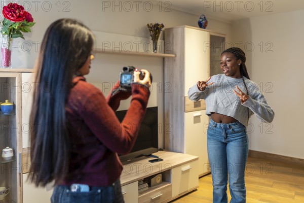 Two teenage girls are having fun at home, one filming the other dancing with a photo camera