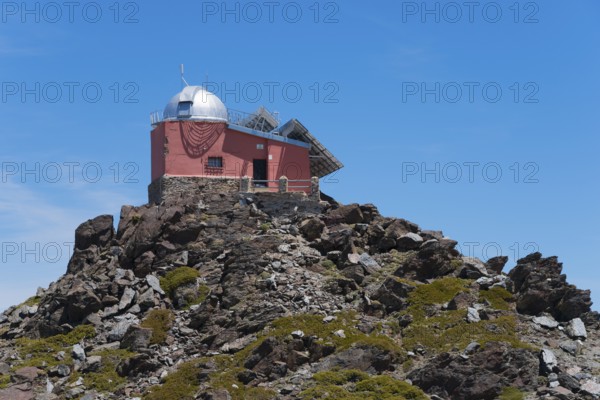 Close-up of a red observatory on a rocky hill under a blue sky, Obversatorium, Mohon del Trigo