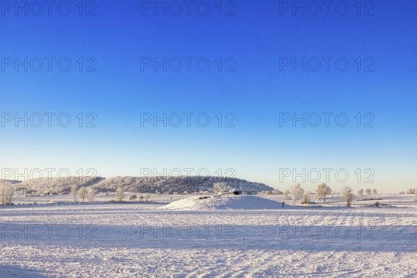Winter landscape with snow and frost in the countryside with a Passage grave on a hill and a table