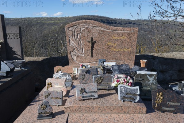 Grabsteine und Blumenschmuck auf einem Friedhof in einer hügeligen Landschaft mit einem