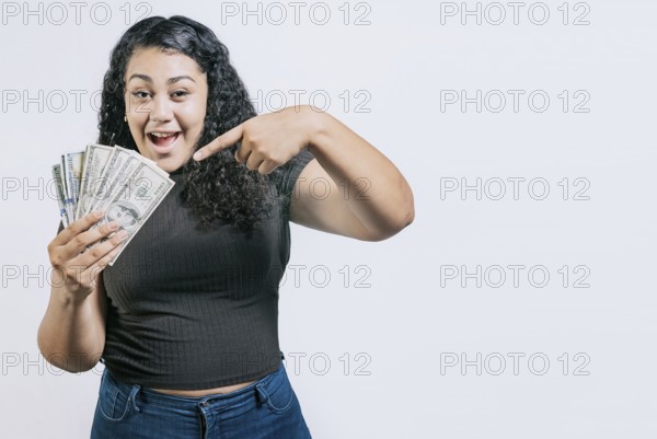 Smiling young woman holding and pointing money isolated. Attractive latin girl holding and pointing