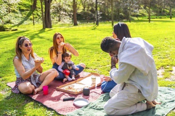 Group of friends savoring delicious pizza while enjoying a sunny picnic in a vibrant park,