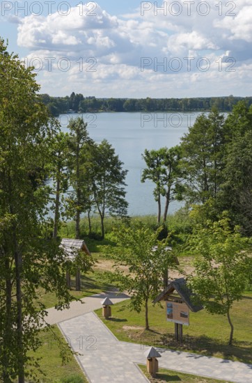 Lake with surrounding trees and well-kept path under a blue sky with clouds, view from the