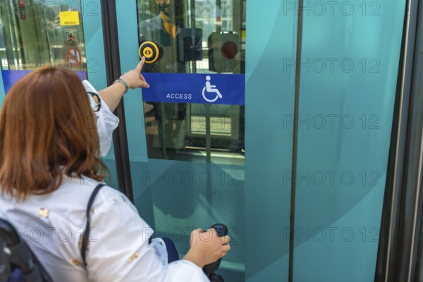 Woman using a wheelchair is pushing accessible button to enter public transport, promoting