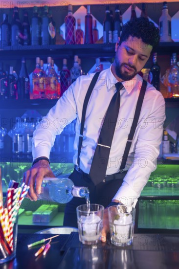Professional bartender preparing cocktails, pouring alcoholic beverage into glasses with ice at bar