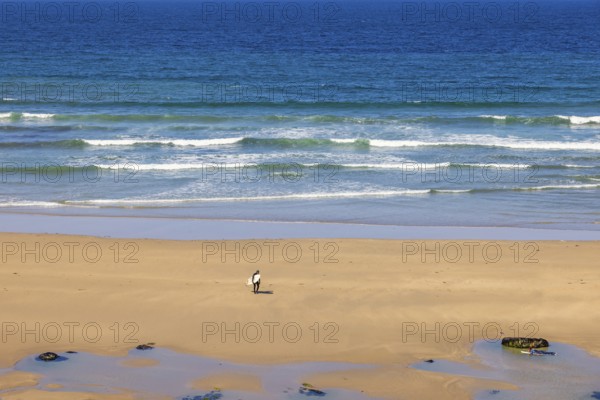 Man with a surfboard walking up from the water with breaking waves on a sand beach, Crozon