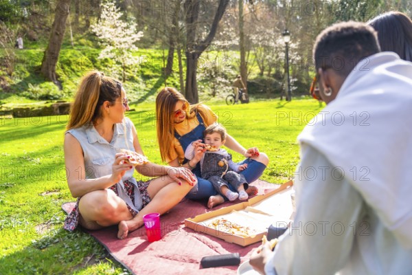 Group of friends and family members are sitting on blanket, eating pizza and enjoying sunny spring