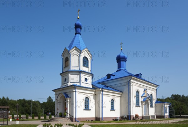 Orthodox church with a blue roof and white facades under a clear sky in a summer landscape,