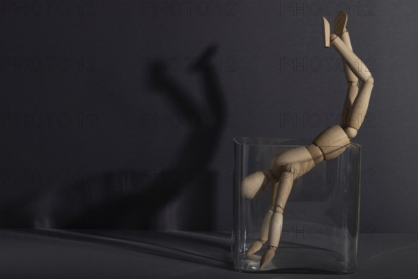 Wooden mannequin in a glass cube on gray background. captivity, break rules, loneliness, depression