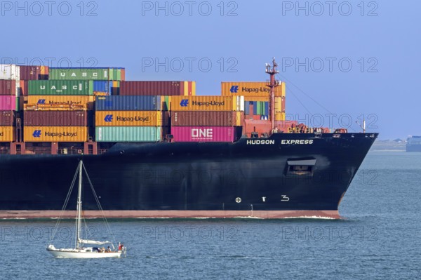 Sailboat sailing past bow of container ship, containership Hudson Express of the Hapag-Lloyd AG