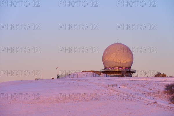 A radar station radome on a snow-covered hill at sunset with pink sky, winter, Wasserkuppe,